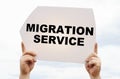 Against the background of the sky in the hands of a man is a sign with the inscription - Migration Service Royalty Free Stock Photo
