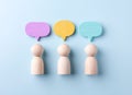 Against a blue backdrop, three wooden figures stand under vibrant speech bubbles, symbolizing the exchange of ideas, communication Royalty Free Stock Photo