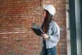 Against brick wall. Young woman is standing in the unfinished building on construction site and working on a project Royalty Free Stock Photo