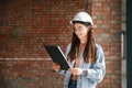 Against brick wall. Young woman is standing in the unfinished building on construction site and working on a project Royalty Free Stock Photo