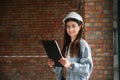 Against brick wall. Young woman is standing in the unfinished building on construction site and working on a project Royalty Free Stock Photo