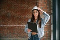 Against brick wall. Young woman is standing in the unfinished building on construction site and working on a project Royalty Free Stock Photo