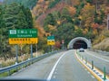 Against colourful autumn trees, signs on the approach to the 1,610m long Maki Tunnel, Japan