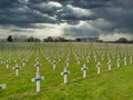 Against dark, threatening skies, rows of graves of WW1 soldiers marked by white crosses in La Targette cemetery near Arras in