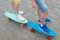 Against the stone paving, close-up, two skateboards with the feet of a boy and a girl on them