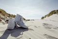 Against sunshine view on pair of white ankle sneakers laying on sand dune. North sea coastal landscape Royalty Free Stock Photo