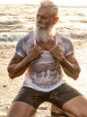 Age is just a number! In healthy body - healthy mind. Handsome fit muscular senior posing in the ocean at sunset time