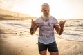 Age is just a number! In healthy body - healthy mind. Handsome fit muscular senior posing on the beach at sunset time