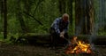 Aged bald forester is burning campfire in woodland correcting firewoods by stick Royalty Free Stock Photo