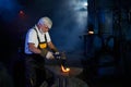 Aged blacksmith forging steel on anvil with heavy hammer