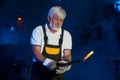 Aged blacksmith holding heated steel with forceps at forge