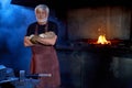 Aged blacksmith in safety apron and gloves posing at forge