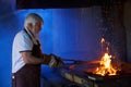 Aged blacksmith in safety gloves tempering steel in stove