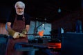 Aged blacksmith working at forge with heated metal