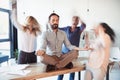 Aged businessman sitting on table and meditating in lotus position while colleagues running around Royalty Free Stock Photo