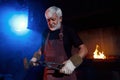 Aged blacksmith using hammer and forceps for work with metal