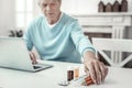 Aged concentrated man using the laptop holding hand near pills. Royalty Free Stock Photo