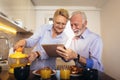 Senior couple busy look at digital tablet while having delicious breakfast at home kitchen Royalty Free Stock Photo