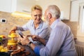 Senior couple busy look at digital tablet while having delicious breakfast at home kitchen Royalty Free Stock Photo