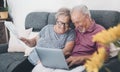 Aged couple at home paying bills on line with laptop and laughing a lot having fun together. Happiness and elderly lifestyle. Man