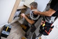 Aged electrician, repairman in uniform working, examining cable, checking voltage in fuse box using multimeter while his