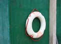 Aged faded red and white plastic lifebuoy hanging on the wall of a vintage green door Royalty Free Stock Photo