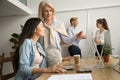 Aged female mentor helping asian girl intern explaining computer