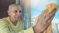 Aged grayhaired man washing window glass with yellow rag Royalty Free Stock Photo