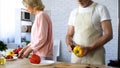 Aged husband and wife holding fresh vegetable, cooking dinner together at home