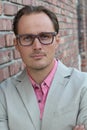 Aged imposing businessman in beige suit and pink dress shirt with arms crossed on chest. Isolated on urban brick wall background