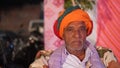 Aged Indian man in traditional dress with colorful turban sitting on sofa and looking at camera