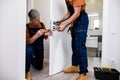Aged locksmith, repairman, worker in uniform installing, working with house door lock using screwdriver while his