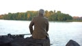 Aged male sitting on stone river bank, thinking of life, enjoying nature view Royalty Free Stock Photo
