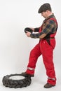 Aged man dressed in red overalls compares a small wheel from a tractor with a large