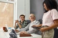 Aged man, senior intern smiling to his young colleague while using laptop, Friendly workers mentoring and training new