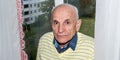 Aged man in yellow pullover stands at white curtains Royalty Free Stock Photo