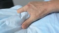 Aged patient squeezing sheets suffering strong pain, serious illness, convulsion