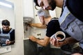 Aged plumber, repairman in uniform fixing electric boiler with wrench while his young colleague helping him, holding