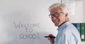 Aged professor writing welcome to school on white board and smiling at camera Royalty Free Stock Photo