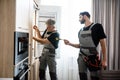 The technical people. Aged repairman in uniform fixing refrigerator in the kitchen, while his colleague helping him