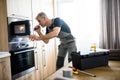 Here for Repairs. Aged repairman in uniform working, examining broken microwave in the kitchen using flashlight. Repair