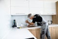 Aged repairman in uniform working, fixing broken kitchen tap using adjustable wrench. Repair service concept