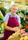 Aged salesman putting onions on food stall in greengrocery