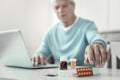 Aged senior man sitting and holding hand near pills. Royalty Free Stock Photo