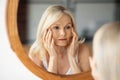 Aged skin problems. Upset senior woman looking at mirror and touching face, lady noticed wrinkles near eyes Royalty Free Stock Photo