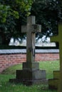 Aged stone cross in a graveyard setting, with a red brick wall in the background Royalty Free Stock Photo