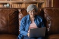 Elderly latin lady sit on sofa hold laptop on knees