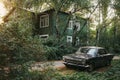Aged vintage soviet black retro car on background of green wooden old house and autumn park