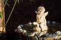 Aged white angel Cupid sculpture sitting water fountain