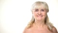 Aged woman with bare shoulders smiling on camera, bodycare concept, cosmetology